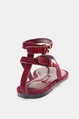 Sandalia plana de serraje color bordó, con tira que separa el dedo gordo y tiras ajustables con hebilla en el tobillo.