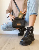 Bandolera de cuero negro con textura grabada tipo cocodrilo en el frente y laterales lisos. Cuenta con doble compartimento con cierre metálico, correa larga ajustable y etiqueta de cuero natural con logo grabado.
