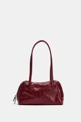 Bolso de hombro de piel con formato bowling, acabado texturizado tipo cocodrilo y color bordó. Cuenta con doble asa de hombro, cierre principal de cremallera con doble tirador y bolsillo interior con cremallera.