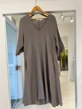 Vestido midi color visón con cuello en V, mangas tres cuartos y corte amplio y fluido con bolsillos laterales.