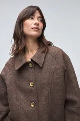 Chaquetón de lana fina sin teñir, con cuello camisero, cierre frontal de botones y bolsillos delanteros. Diseño de corte recto y estructura clásica.