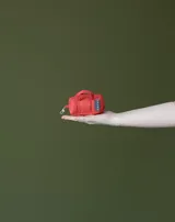 Charm en forma de mini bolso tipo duffel color rojo, con asas cortas, etiqueta con logo y cierre con mosquetón.