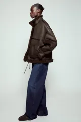 Chaqueta bomber de cuello alto con forro interior de pelo sintético. Presenta cierre frontal con botones, bolsillos delanteros y bajo ajustable con cordones.