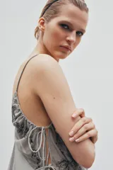 Top de tul con escote en pico y tirantes finos. Presenta bordados florales con aplicación de lentejuelas y laterales ajustables mediante lazadas.