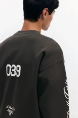 Buzo verde militar de corte oversized, confeccionado en mezcla de algodón con cuello redondo, puños y dobladillo acanalados. Cuenta con estampados en el frente, la espalda y las mangas, incluyendo inscripciones y estrellas.