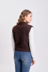 Chaleco de punto en color marrón, con cuello alto y diseño sin mangas. Presenta un tejido de punto liso y corte holgado.