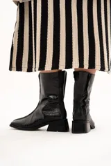 Bota de caña media color negro con textura de reptil, confeccionada en cuero. Presenta horma cuadrada, cierre lateral interno, taco cuadrado y una pequeña plataforma.