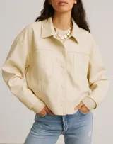 Sobrecamisa color crudo, de corte recto, con cuello camisero, cierre frontal con botones a tono, mangas largas con puños abotonados, bolsillos de parche en el pecho y confeccionada en simil cuero.