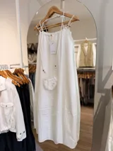 Vestido midi celeste de silueta amplia y fluida, con escote fruncido y tirantes finos decorados con cuentas de madera. Incluye una pequeña carterita colgante haciendo juego.