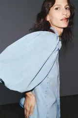 Camisa de denim celeste con cuello solapa, manga corta abullonada y cierre frontal con botones.