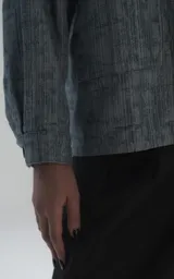 Campera de denim rígido con textura de trama única, corte oversize, cuello camisero, cierre frontal con botones y bolsillos delanteros con solapa.