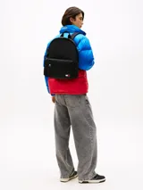 Mochila negra de diseño redondeado con acabado texturizado. Cuenta con un compartimento principal amplio, un bolsillo exterior con cremallera y un bolsillo interior de malla abierto. Tiene asas ajustables y acolchadas, asa superior y un parche tejido con el logo de Tommy Jeans en la parte delantera.