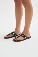 Ojotas negras con tira ancha entre los dedos, decoradas con apliques metálicos plateados en relieve.