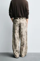 Pantalón de corte relajado confeccionado en algodón, con diseño de efecto lavado y estampado abstracto en tonos grises y beige. Presenta cinco bolsillos y cierre frontal con cremallera y botón.