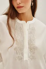 Camisa de algodón color blanco, con cuello redondo, cierre frontal parcial con botones y detalle de bordado con canutillos en el frente.