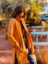 Tapado camel de cuero ovino con cuello clásico, cierre frontal con botones, bolsillos laterales y corte a la rodilla. Diseño slouchy y cómodo.