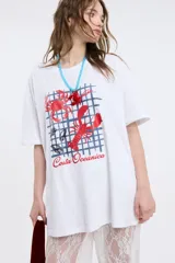 Remera blanca de corte oversize con cuello redondo y mangas cortas. Presenta una estampa frontal con diseño de cuadrícula azul, motivos marinos en color rojo como cangrejos y langostas, y la inscripción 'Costa Oceánica'.