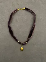 Choker de cinta de terciopelo color ciruela con dije central en forma de escarabajo dorado con incrustaciones de cristales y detalles metálicos en los extremos.