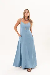 Vestido largo de denim fino y liviano, color celeste, con breteles finos, escote delicado, silueta entallada en la parte superior, falda amplia con recortes verticales y bolsillos laterales.