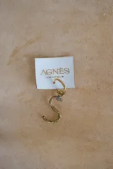 Aro individual dorado con dije colgante en forma de letra "G" con textura irregular.