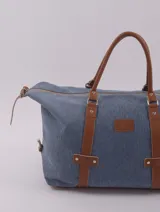 Bolso de viaje tipo duffle, confeccionado en cuero natural color azul con textura, con detalles de correas y asas en cuero color suela. Cuenta con cierre superior, bolsillo interior con cierre y compartimento para celular.