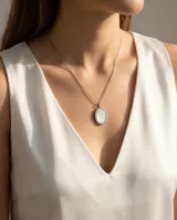 Collar de cadena fina de acero con dije ovalado de nácar engarzado en metal plateado.