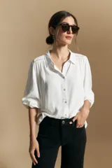 Camisa de manga larga con cuello clásico y cierre frontal de botones. Presenta detalles de vainilla en los hombros y puños elásticos con volados. De calce fluido y caída liviana.