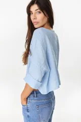 Camisa de lino azul marino, de corte crop y holgado, con cuello redondo, botonadura frontal y mangas amplias con vuelta.