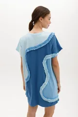 Vestido corto de algodón, con bloques de color en tonos pastel (amarillo claro, beige y rosado pálido) unidos por volados fruncidos en tonos marrón claro y amarillo. Presenta cuello redondo y mangas cortas.