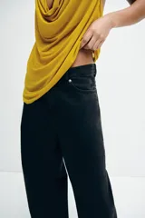 Jean de tiro alto y estilo baggy color negro, confeccionado en denim de algodón rígido, con diseño de cinco bolsillos, cierre de cremallera y botón metálico, y perneras amplias de corte holgado.