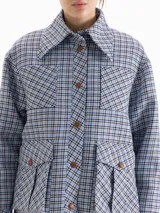Chaqueta de twill en tono celeste con estampado de cuadros, corte camisero y largo por debajo de la cadera. Presenta cuello clásico, cierre frontal con broches forrados en cuero y bolsillos frontales tipo cargo.