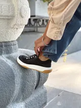 Zapatillas deportivas negras de cuero, con cordones y suela de goma blanca con base marrón.