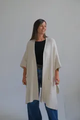Poncho abierto de tejido de punto color crudo, con mangas tres cuartos y bolsillos frontales aplicados.