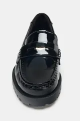 Mocasín de estilo penny en material sintético con acabado acharolado brillante. Presenta un diseño de punta redonda, antifaz clásico en el empeine y una suela dentada robusta.