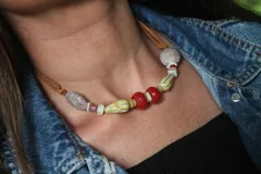 Collar de estilo artesanal con cuentas de piedra, cerámica y vidrio en tonos rojos, amarillos y grises, montado sobre un cordón de cuero ajustable.