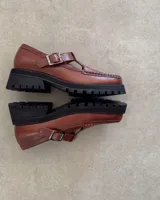 Zapato tipo guillermina marca Lucy in the Sky, confeccionado en cuero vacuno color marrón. Presenta costuras decorativas en el borde superior, cierre con hebilla lateral y suela track negra de goma.