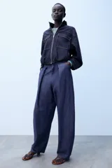 Pantalón confeccionado con lino de tiro alto con pliegues delanteros y cinco bolsillos. Presenta pernera holgada y cierre frontal con cremallera, botón interior y gancho.