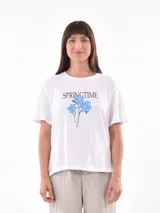 Remera blanca de corte recto y manga corta, con estampa frontal que incluye la palabra SPRINGTIME y un diseño de flores azules.