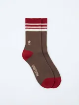 Medias de caña media color marrón con detalles en rojo y blanco. Presentan rayas horizontales en el puño, logo bordado en el tobillo y la palabra UNIFORM estampada en el lateral.