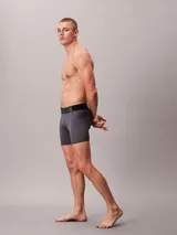 Pack de tres boxers largos Calvin Klein de microfibra, con talle medio y cinturilla elástica distintiva con el logo de la marca. Incluye un bóxer negro con elástico negro y letras blancas, un bóxer gris con elástico negro y letras grises, y un bóxer azul con elástico negro y letras azules.