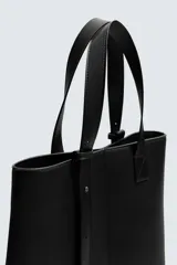 Bolso tipo shopper de diseño minimalista en color negro, con estructura vertical, doble asa de hombro y detalle de tira decorativa frontal con cierre magnético.