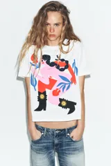 Remera blanca de corte oversize con cuello redondo y mangas cortas. Presenta un estampado artístico a color en el frente que ilustra una figura femenina estilizada con botas estilo western.