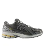 Championes urbanos New Balance modelo 1906R, color gris con detalles en amarillo y negro. Presentan una estructura técnica con paneles de malla y refuerzos sintéticos, logo N lateral y entresuela con tecnología de amortiguación.