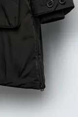 Parka técnica de corte relajado con acabado repelente al agua. Presenta cuello subido con capucha ajustable, cierre frontal con cremallera oculta por solapa con botones y cintura ajustable con cordón. Incluye múltiples bolsillos frontales con solapa, un bolsillo con cremallera en la manga y puños con interior en rib. El diseño cuenta con interior acolchado y aberturas laterales con cremallera en el bajo.