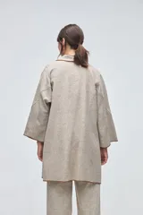 Tapado de largo medio abierto con cuello, confeccionado en lana fina sin teñir con detalles de terminación envivados en los bordes y mangas tres cuartos.