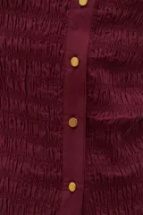 Camisa de manga corta en color bordó, confeccionada en tejido con textura de punto smock. Presenta cuello clásico, cierre frontal con botones y un ajuste entallado al cuerpo.