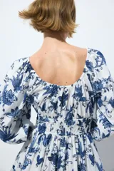 Vestido corto de algodón con estampado floral en tonos azules sobre base blanca, escote en V y mangas globo de longitud al codo. Presenta elástico fruncido en el pecho y la cintura, con falda evasé de vuelo.