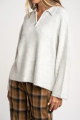 Sweater de punto en color gris melange, con diseño oversize, cuello polo y cierre frontal parcial. Presenta mangas largas y una textura acanalada suave.