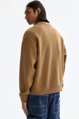 Buzo marrón de algodón con cuello redondo, hombros caídos y diseño estampado en el frente con la inscripción 'SOHO NYC ATHLETICS DEPT.' en color beige. Presenta puños y bajo de canalé elástico.