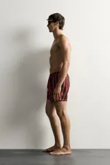 Short de baño confeccionado en tejido técnico, con diseño de rayas verticales en color verde y negro. Cuenta con cintura elástica ajustable con cordón, bolsillos laterales y bolsillo trasero con vivo, además de forro interior.